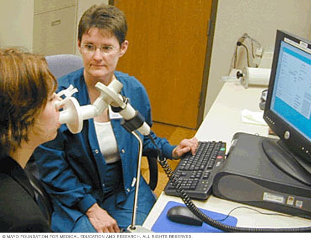 Mujer usando un espirómetro, asistida por un técnico