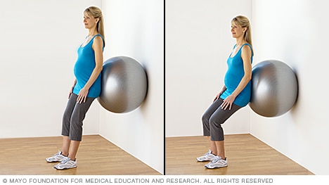 امرأة حامل تمارس تمرين القرفصاء وتستخدم كرة اللياقة البدنية