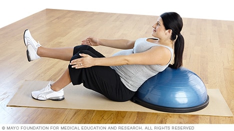 Persona embarazada haciendo el ejercicio de abdominales en V, apoyada en una plataforma de equilibrio