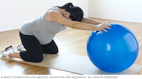 امرأة حامل تمارس تمرين إطالة عضلات الظهر باستخدام كرة اللياقة البدنية