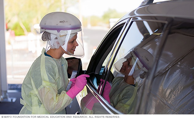 ممرضة تتحدث مع سائق في أحد مواقع فحص كوفيد-19 من السيارة.