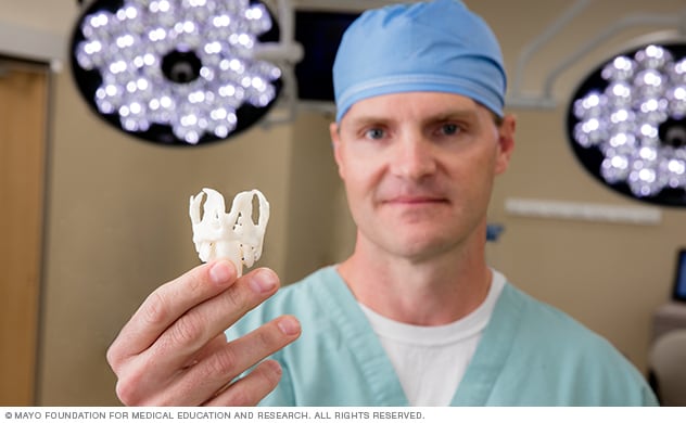 A surgeon holds up a 3D-printed larynx in an operating room.