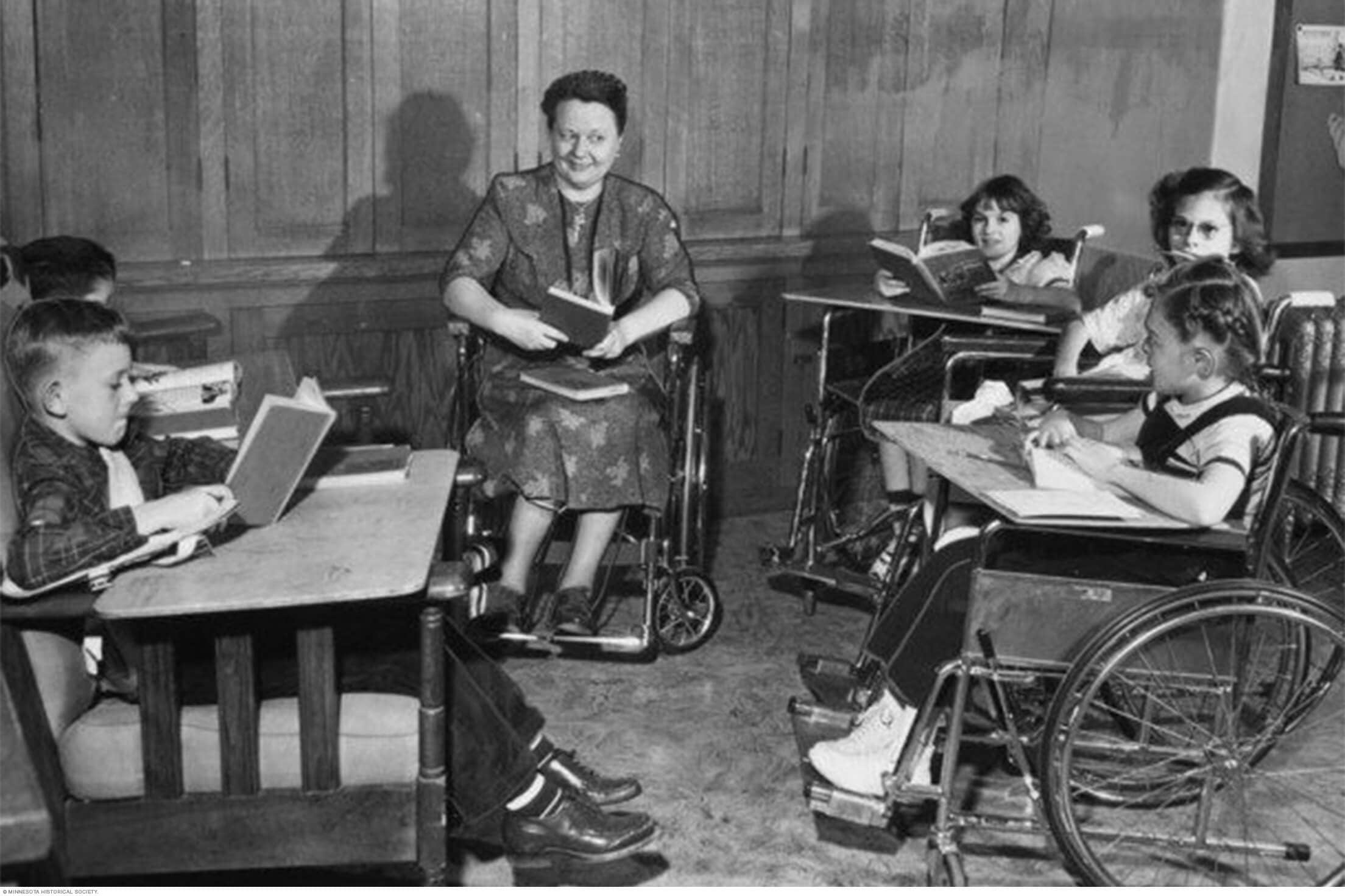 Niños y personal docente en sillas de ruedas con libros y libretas en una clase en el hospital Saint Mary
