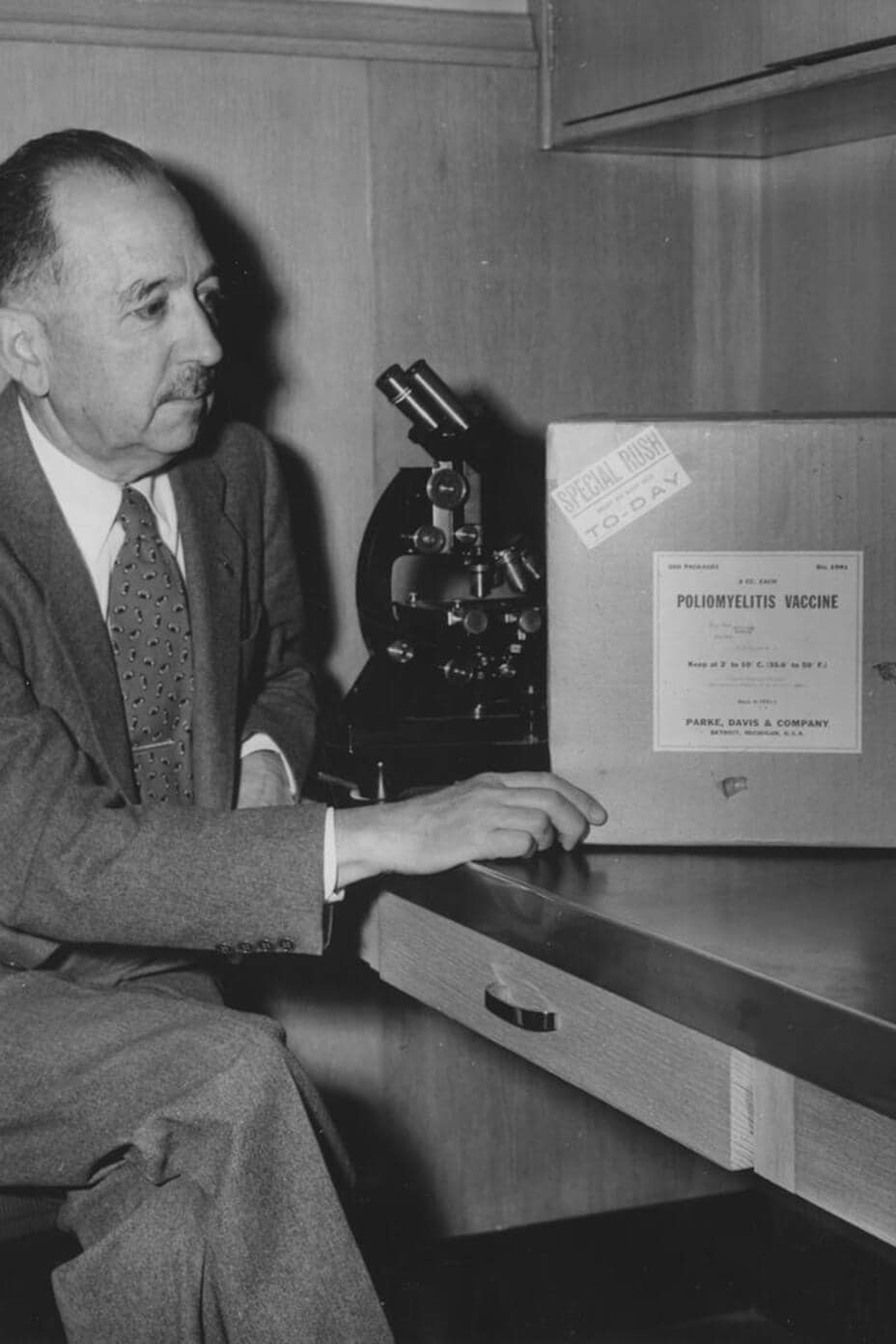 El Dr. Thomas Magath sentado en un escritorio mientras observa el primer envío de vacunas contra la poliomielitis en Mayo Clinic en 1955