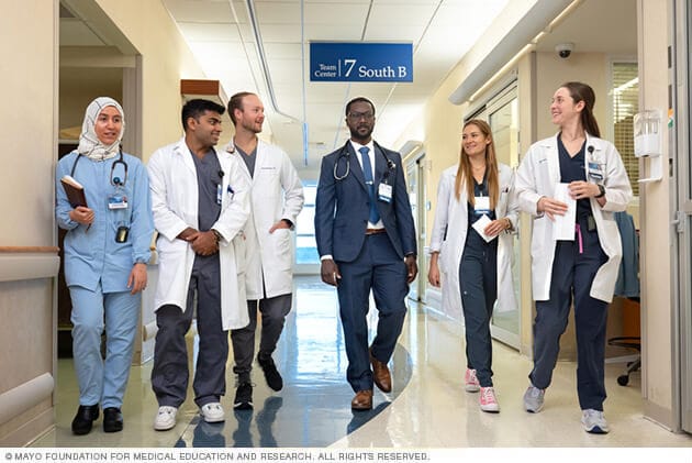 A Mayo Clinic medical team converses walking through a hospital hallway.