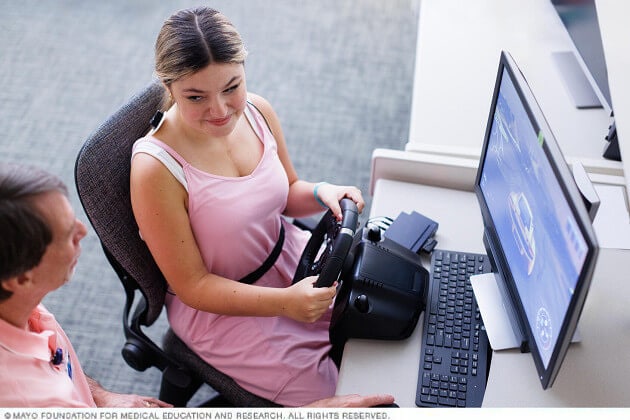 A young woman participates in a biofeedback session using a video monitor and console.